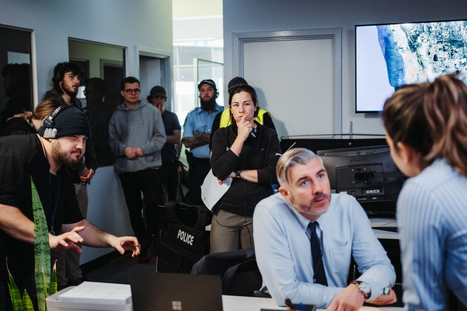 Kelly watching a take with cast and crew on a police-office set